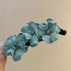 Détail d'une pince à cheveux en tissu bleu-gris montrant les pétales superposés