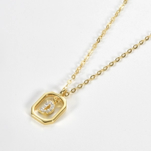 Detail of gold necklace featuring a rectangular pendant with crystal letter D inlay