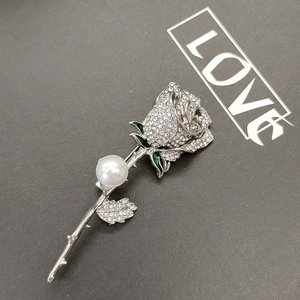Detailed close-up of a silver rose brooch with pavé rhinestones and a white pearl