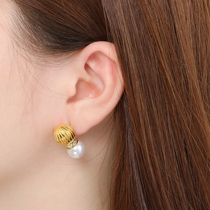 Close-up of a model wearing a golden pumpkin-shaped stud earring with a white pearl drop
