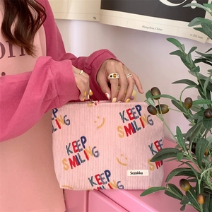 Detail of pink corduroy makeup bag featuring colorful Keep Smiling text and smiley faces