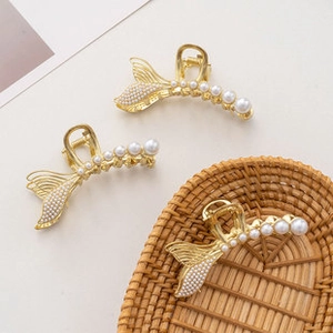 Golden fishtail hair claw clip with elegant white pearls on a minimalist background