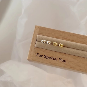 Minimalist s925 silver heart stud earrings in gold and silver finish on a wooden box
