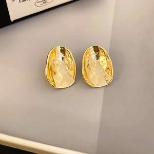 Macro detail of golden hammered irregular stud earrings with polished metallic texture