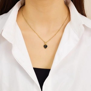 Detail of gold beaded chain necklace featuring a black enamel heart pendant on a model
