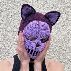 Macro detail of handmade crochet balaclava featuring cat ears and purple skull pattern