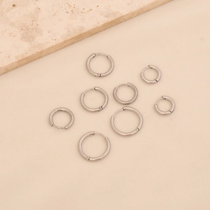 Flat lay of eight silver stainless steel hoop earrings in various sizes on beige surface