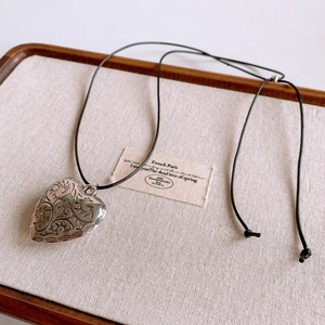 Detailed macro view of vintage engraved heart pendant with black wax cord on a wooden tray