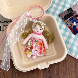 Detail of floral plush doll keychain with lace ribbon and golden hair in gift box