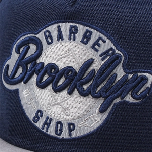Détail macro de la broderie 3D Barber Shop sur une casquette en sergé de coton bleu