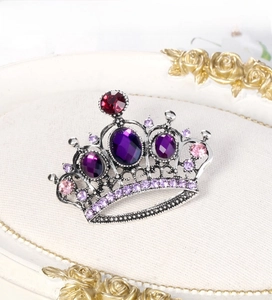 Detail of a vintage crown brooch with purple and red rhinestones on a silver base