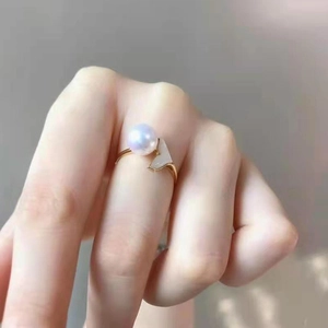 Elegant gold pearl ring with white shell fin design on fingers against grey background