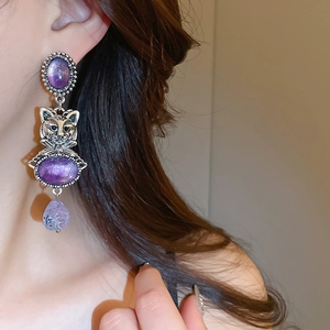 Detail view of vintage silver earrings featuring purple stones and cat head charms
