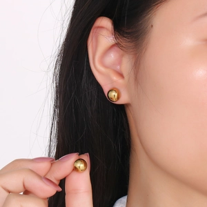 Chic golden spherical stud earrings in polished stainless steel on female model