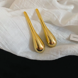 Macro view of large golden teardrop earrings with mirror finish on white fabric