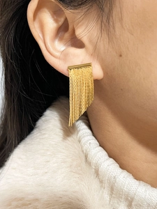 Detailed close-up of long gold fringe tassel earrings worn on a model with white collar