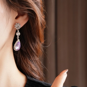 Detailed view of silver teardrop purple zircon earrings with crystal floral cluster on model