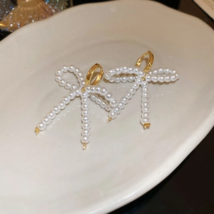 Élégantes boucles d'oreilles nœud dorées avec perles blanches sur un plat en céramique
