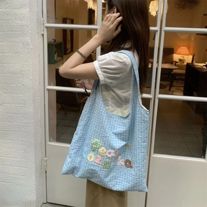 Detail of light blue checkered tote bag featuring colorful peach soza ka letter embroidery