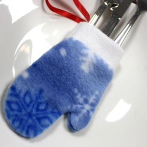 Blue felt Christmas glove cutlery holder with white snowflake pattern on a ceramic plate