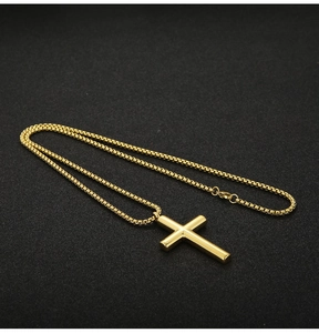 Close-up of golden stainless steel cross pendant with polished box chain on dark background