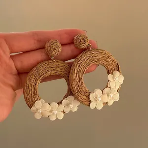 Bohemian rattan hoop earrings with white gauze flowers and pearl centers on brown background