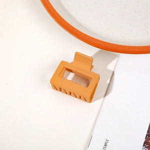Close-up of a matte orange rectangular hair claw clip on a minimalist white surface