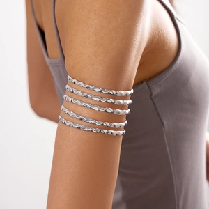 Detail of a layered silver arm cuff with wavy texture and polished finish on model