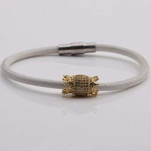 Detail of white cord bracelet featuring a gold crown-edge barrel bead set with cubic zirconia