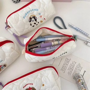 Close-up detail of a quilted pencil case with cute puppy embroidery and stationery inside