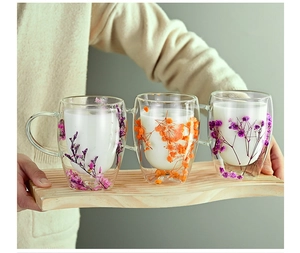 Close-up of double-walled glass mugs with dried flowers being held on a wooden tray