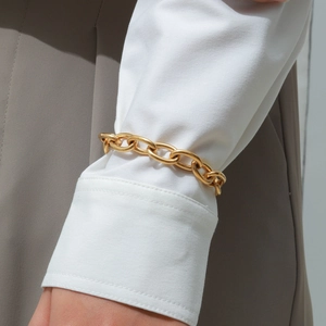 Detail of chunky gold chain bracelet with OT toggle clasp worn over a white shirt sleeve