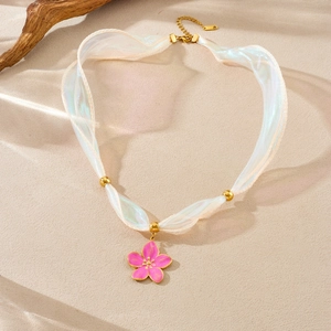 Detail view of pink enamel flower pendant with iridescent white ribbon on a textured surface
