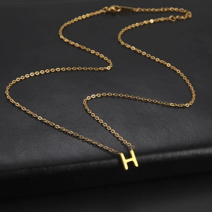 Macro view of gold plated 18k letter H pendant necklace on black textured leather