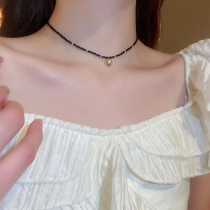 Gros plan d'un collier choker en perles de cristal noir avec un pendentif cœur doré