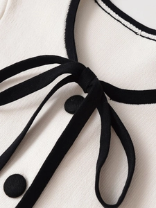 Close-up of white knit top featuring black contrast trim, bow tie, and textured buttons