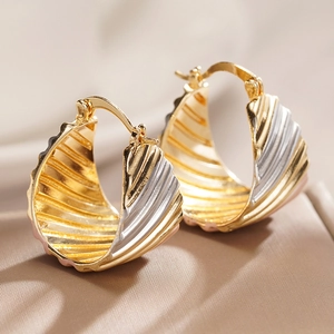 Macro-opname van tweekleurige goud en zilver golvende oorbellen met elegant schelppatroon
