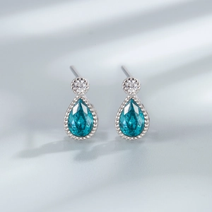 Macro shot of silver drop earrings with teal gemstones on a grey textured background