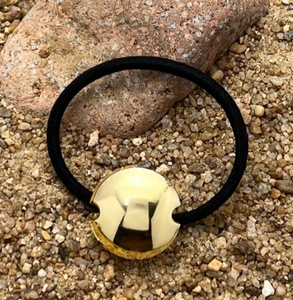 Detail shot of a black elastic hair tie with a gold circular metal charm on natural stones