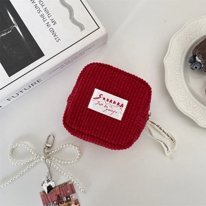 Detail of red corduroy storage pouch featuring a white label and faux pearl bow charm