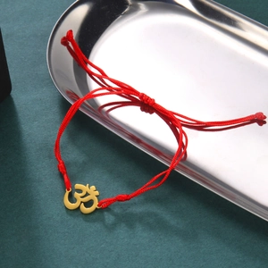 Detail of red braided cord bracelet with golden Yoga Om symbol on a silver tray