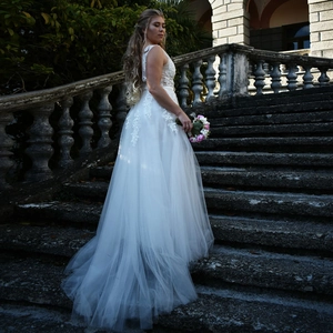 Detail of white V-neck evening gown with lace appliques and multi-layer tulle train