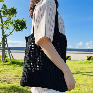 Outdoor close-up of a black crochet mesh tote bag texture with a woven grid design