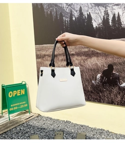 Detail of white handbag with black leather handles and gold metal accents on textured surface