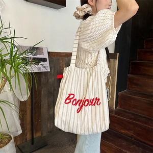 Detailed close-up of red Bonjour embroidery on striped canvas tote bag with soft texture
