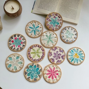 Detail of round rattan coasters featuring colorful mosaic shell patterns on a white table