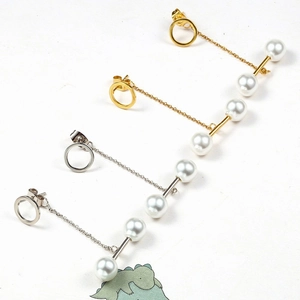 Detailed view of gold and silver tassel earrings with four white pearls on metal chains