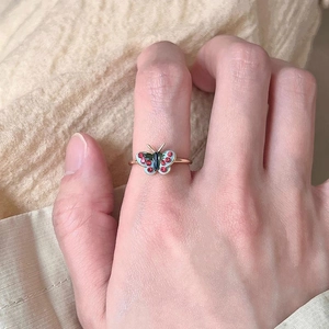 Macro detail of a gold butterfly ring with light blue enamel and red rhinestones