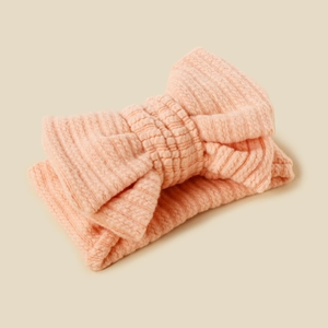 Detailed texture of pink knitted double-layered bow headband for babies on beige background