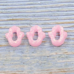 Close-up of three pink Hamsa opal resin charms with iridescent effect on wood surface